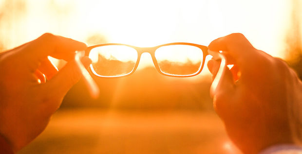 Stock photograph of eyeglasses being held up to a sunset.