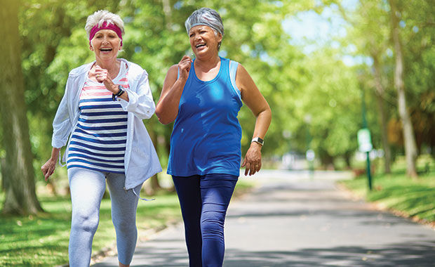 A photograph of two elderly women speed-walking outdoors, smiling and laughing.